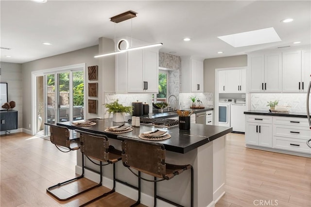 kitchen featuring a breakfast bar, white cabinets, hanging light fixtures, independent washer and dryer, and dark countertops