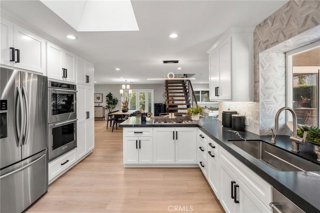 kitchen with a peninsula, white cabinets, stainless steel appliances, and a sink