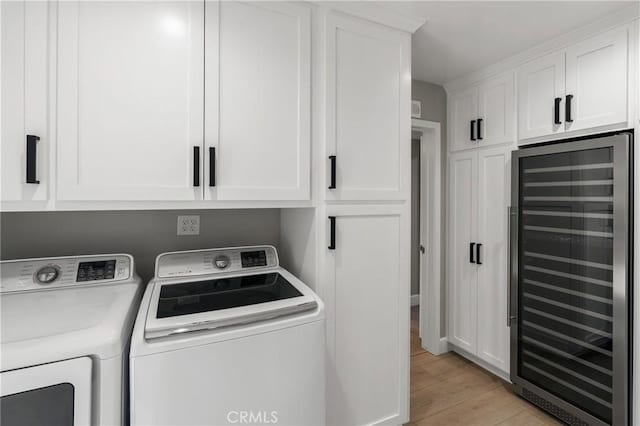 washroom featuring wine cooler, light wood-type flooring, washing machine and dryer, and cabinet space