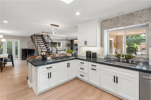 kitchen featuring a peninsula, a sink, white cabinets, open floor plan, and appliances with stainless steel finishes