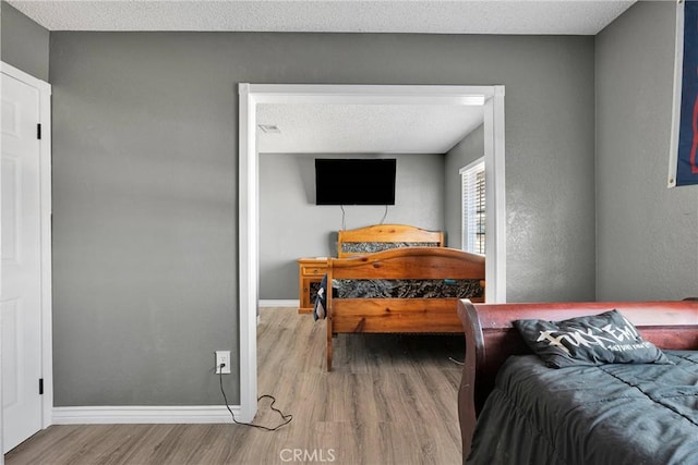 bedroom featuring baseboards, wood finished floors, visible vents, and a textured ceiling