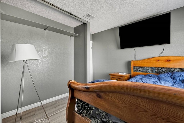 bedroom featuring a textured ceiling, visible vents, wood finished floors, and baseboards