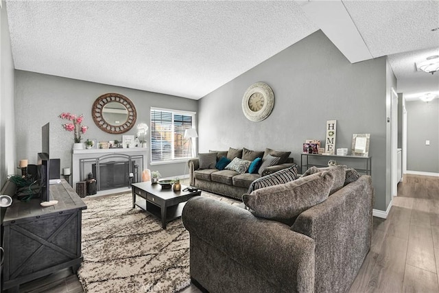 living room with wood finished floors, baseboards, a textured ceiling, vaulted ceiling, and a glass covered fireplace