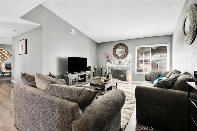 living room featuring light wood-style flooring, baseboards, a textured ceiling, a fireplace, and vaulted ceiling