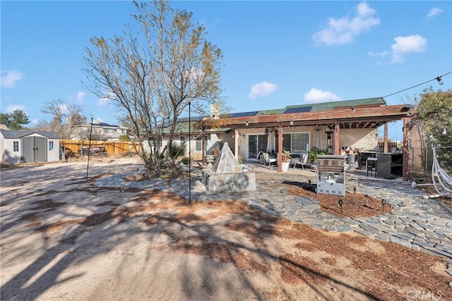 view of front of home with a patio area, fence, roof mounted solar panels, an outdoor structure, and a shed