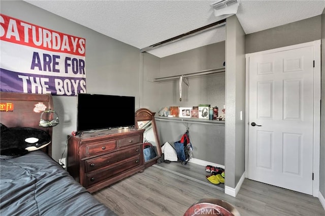 bedroom with baseboards, visible vents, a textured ceiling, and wood finished floors