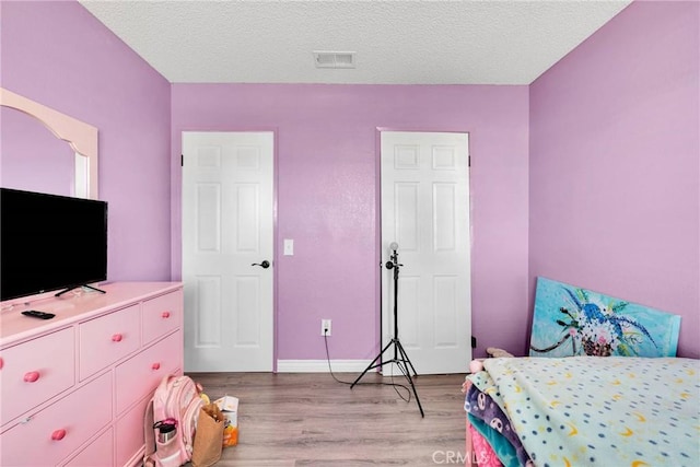 bedroom featuring light wood-style flooring, visible vents, baseboards, and a textured ceiling