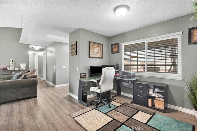 office featuring light wood-type flooring, baseboards, and a textured ceiling