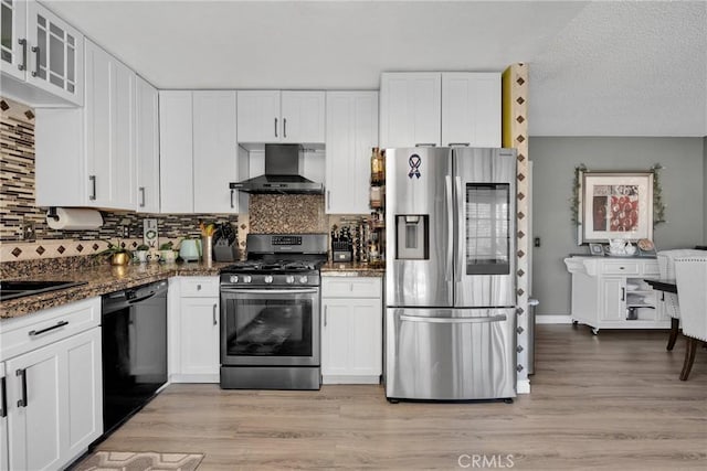 kitchen featuring glass insert cabinets, white cabinetry, appliances with stainless steel finishes, and wall chimney range hood