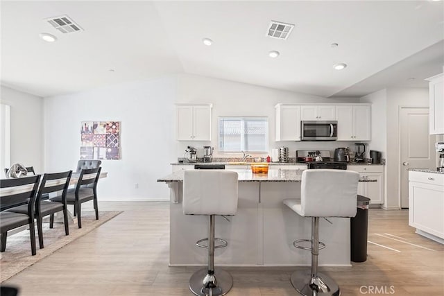 kitchen featuring stainless steel microwave, visible vents, a center island, a breakfast bar, and range