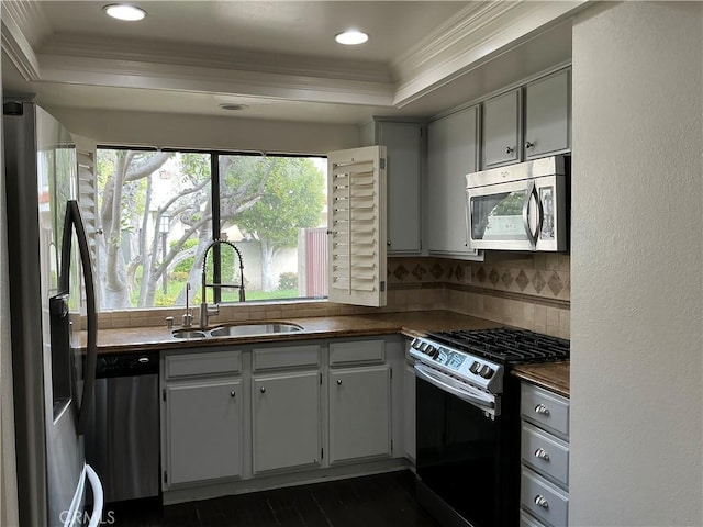 kitchen featuring ornamental molding, a sink, tasteful backsplash, dark countertops, and appliances with stainless steel finishes