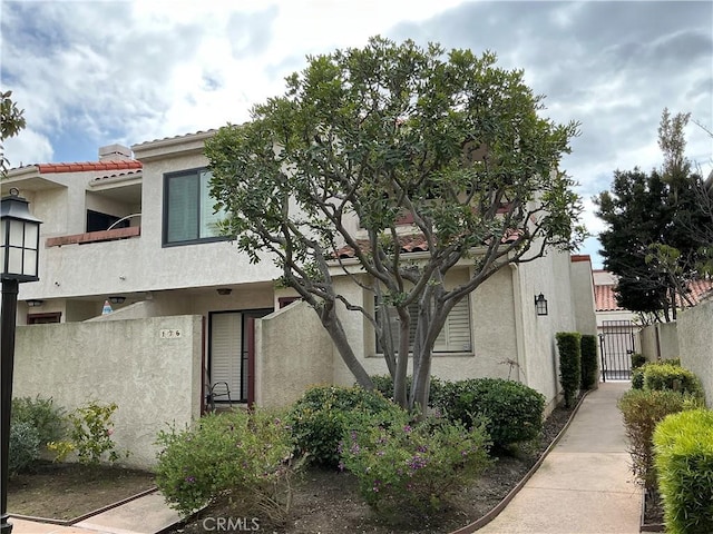 exterior space with stucco siding, fence, a tile roof, and a gate