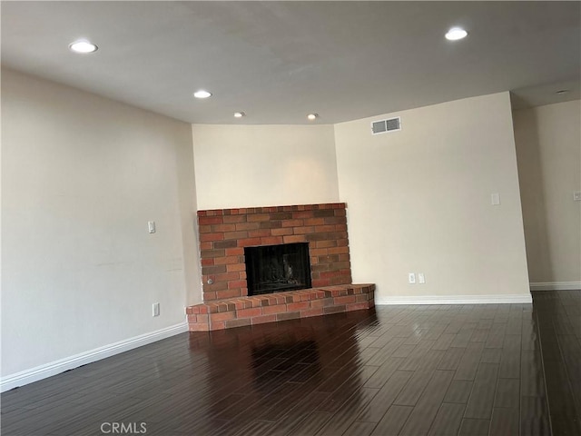 unfurnished living room with dark wood finished floors, a brick fireplace, baseboards, and visible vents