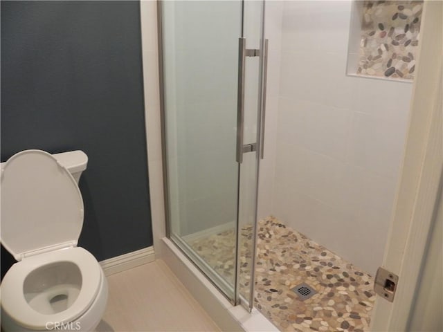 full bathroom with a shower stall, toilet, and baseboards