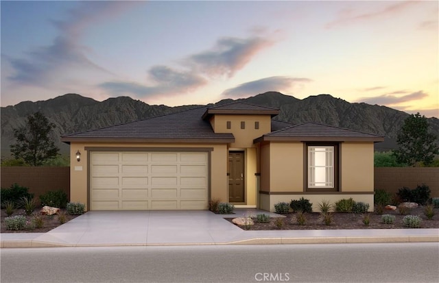 prairie-style home featuring concrete driveway, stucco siding, a mountain view, and a garage