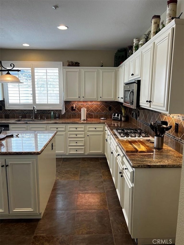 kitchen featuring white cabinetry, gas cooktop, dark stone counters, and sink