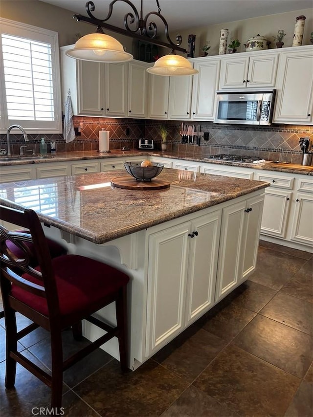 kitchen featuring appliances with stainless steel finishes, pendant lighting, light stone countertops, and a center island