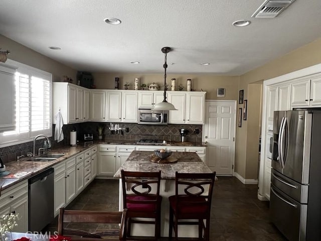 kitchen with stainless steel appliances, a kitchen island, sink, decorative backsplash, and pendant lighting