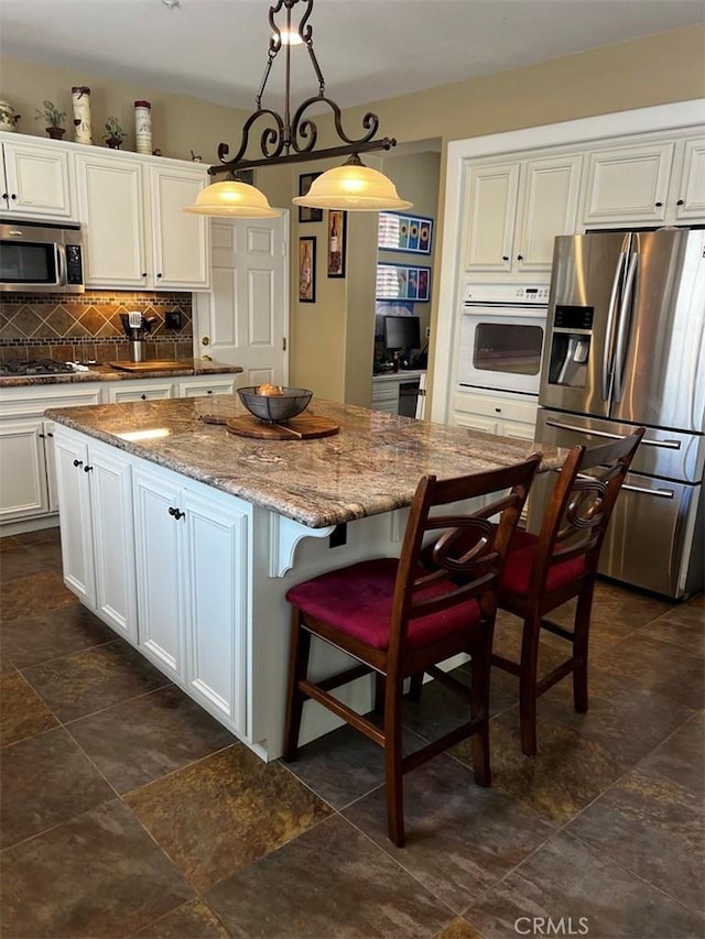 kitchen featuring a kitchen island, light stone countertops, stainless steel appliances, and decorative light fixtures