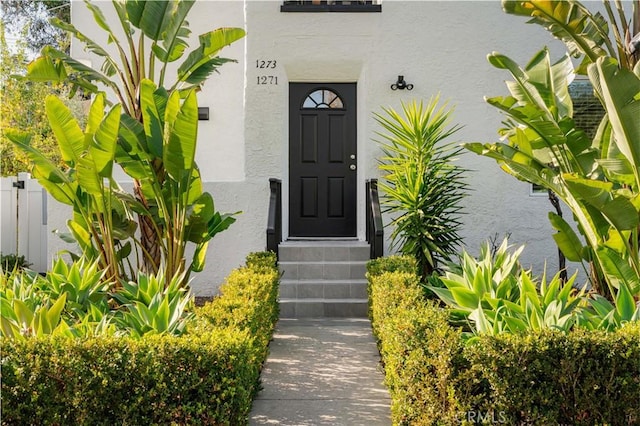 entrance to property featuring fence and stucco siding