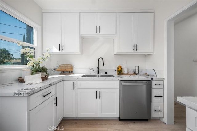 kitchen featuring light stone counters, light wood finished floors, stainless steel dishwasher, white cabinetry, and a sink