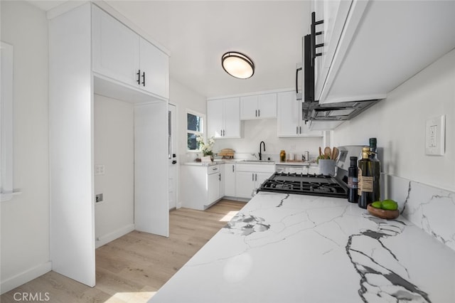 kitchen featuring light stone counters, stove, a sink, white cabinets, and light wood-type flooring