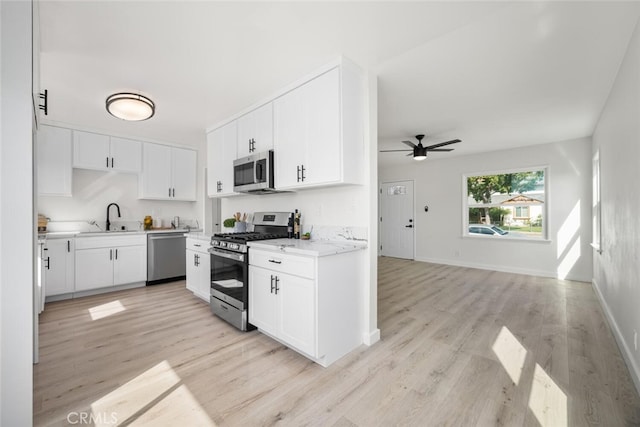 kitchen with appliances with stainless steel finishes, a sink, light wood-style flooring, and white cabinets