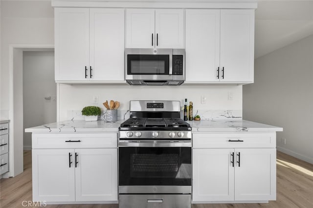 kitchen featuring appliances with stainless steel finishes, light wood-style floors, white cabinetry, light stone countertops, and baseboards