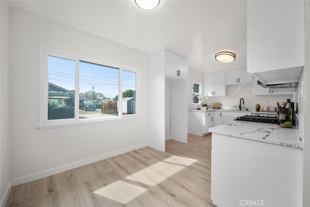 kitchen featuring baseboards, light stone counters, light wood-style floors, white cabinetry, and a sink