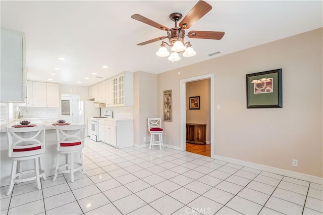 kitchen featuring white cabinets, a breakfast bar area, decorative backsplash, and white range