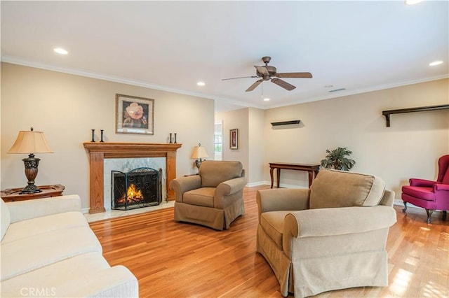 living room with light wood-type flooring, a high end fireplace, ornamental molding, and ceiling fan