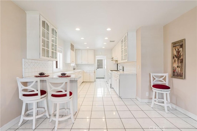 kitchen with sink, white gas range oven, white cabinets, a breakfast bar area, and tasteful backsplash