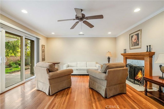 living room with a fireplace, ceiling fan, light wood-type flooring, and crown molding