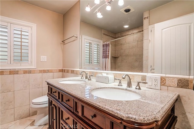 bathroom featuring tile patterned floors, toilet, tile walls, vanity, and walk in shower