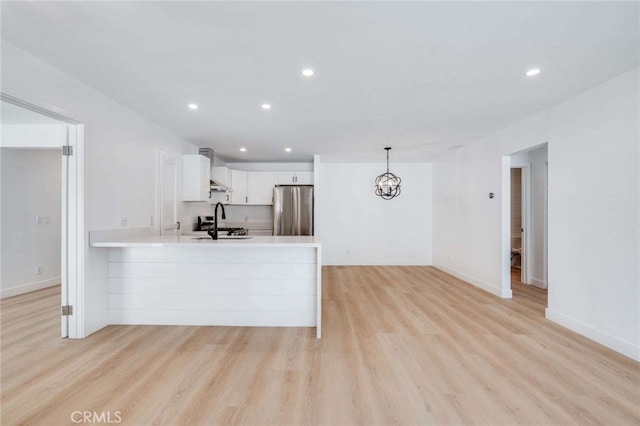 kitchen featuring white cabinetry, kitchen peninsula, hanging light fixtures, stainless steel refrigerator, and sink