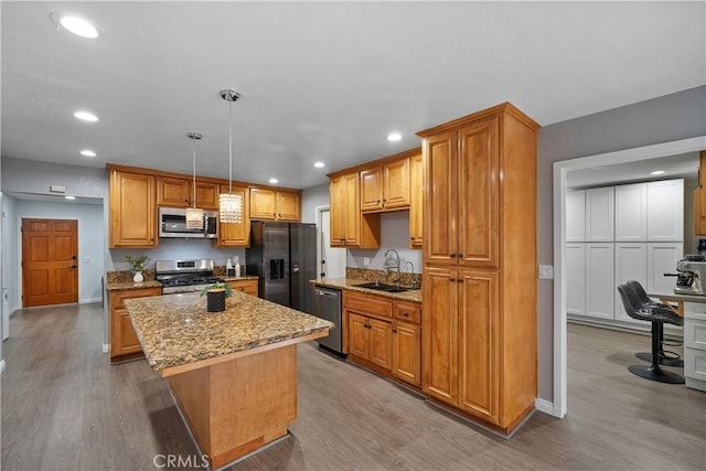 kitchen with a kitchen island, appliances with stainless steel finishes, decorative light fixtures, light wood-type flooring, and a sink