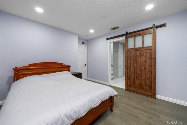 bedroom featuring a barn door, recessed lighting, wood finished floors, visible vents, and baseboards