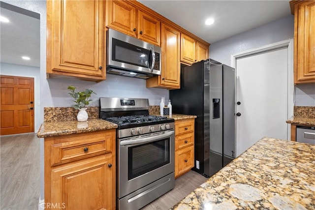 kitchen featuring stainless steel appliances, brown cabinetry, light wood-style flooring, and light stone countertops