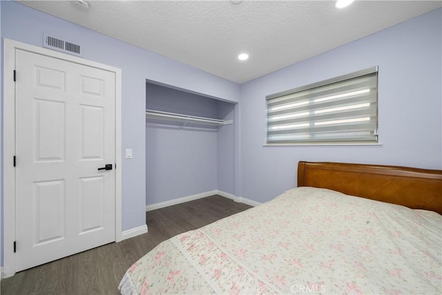 bedroom with baseboards, visible vents, dark wood-style floors, a textured ceiling, and a closet