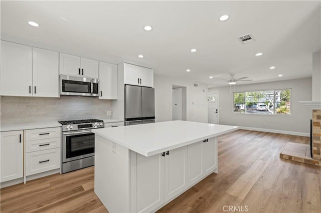 kitchen featuring light countertops, backsplash, appliances with stainless steel finishes, white cabinets, and a kitchen island