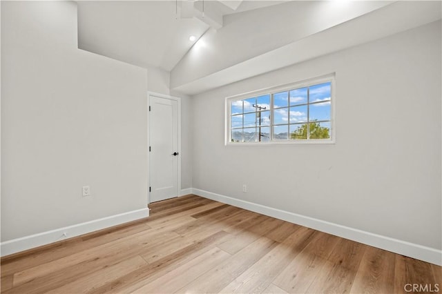 spare room featuring vaulted ceiling with beams, light wood-style floors, and baseboards