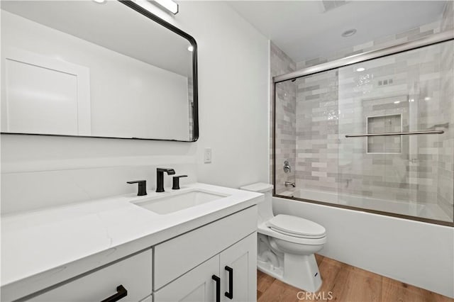 full bath featuring toilet, bath / shower combo with glass door, wood finished floors, and vanity