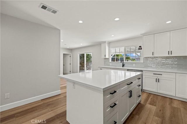 kitchen with visible vents, white cabinetry, light countertops, a center island, and tasteful backsplash