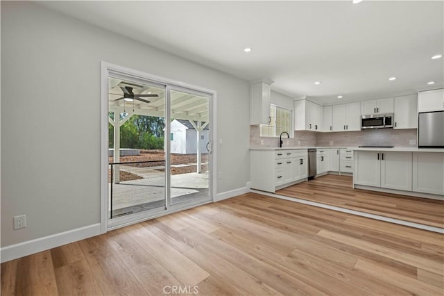 kitchen with stainless steel appliances, white cabinetry, light wood-style floors, light countertops, and backsplash