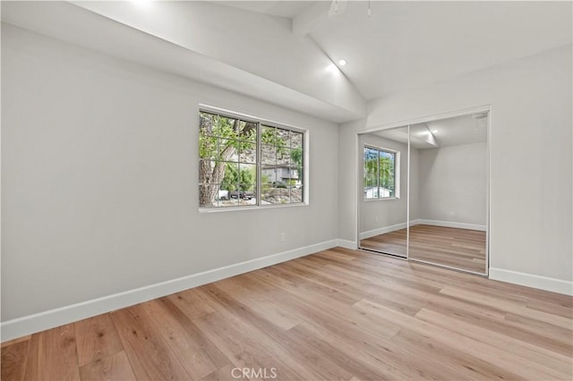 unfurnished bedroom featuring lofted ceiling with beams, light wood finished floors, a closet, and baseboards