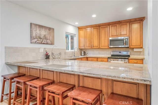 kitchen featuring a sink, appliances with stainless steel finishes, light stone counters, and a peninsula