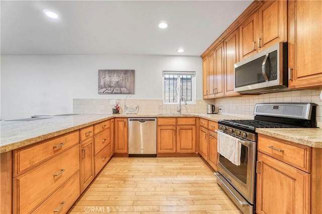 kitchen with stainless steel appliances, light stone counters, a sink, and decorative backsplash