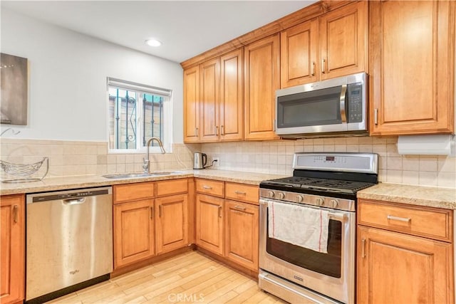 kitchen with light wood finished floors, a sink, light stone countertops, stainless steel appliances, and backsplash