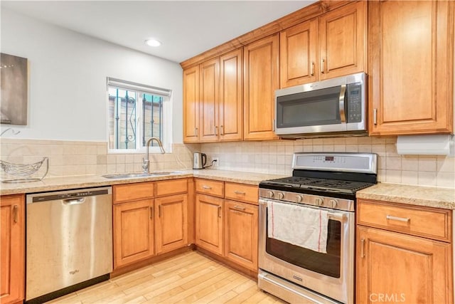 kitchen featuring light wood-style flooring, light stone countertops, stainless steel appliances, a sink, and backsplash