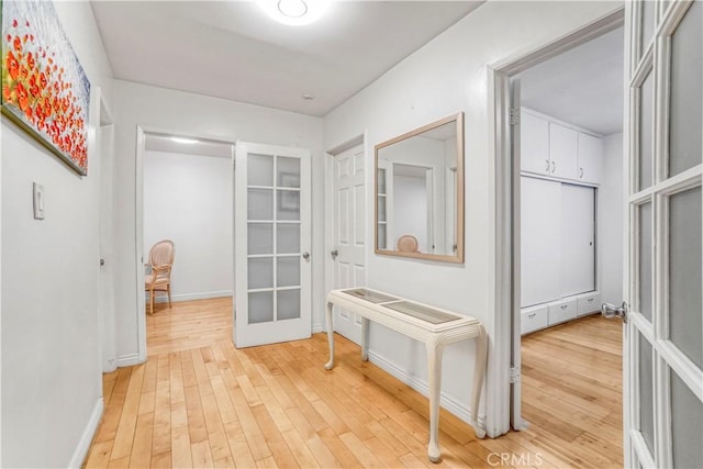 hallway featuring baseboards, light wood-style flooring, and french doors